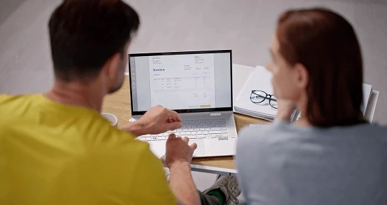 Pracownicy biurowi przeglądający elektroniczną fakturę na komputerze w ramach wdrażania nowego systemu.